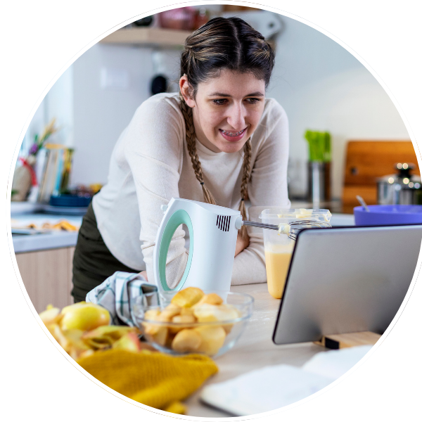 photo of a person looking at a laptop while cooking in the kitchen for a link to online classes webpage